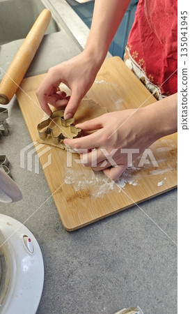 Hands cutting cookie dough with metal cutter on wooden board in home kitchen. This image represents homemade baking process creativity and traditional cooking Hands cutting cookie dough with metal cutter on wooden board in home kitchen. This image represents homemade baking process creativity and traditional cooking 135041945