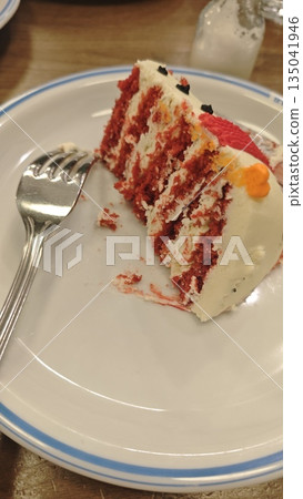 Slice of red velvet cake with cream frosting served on plate with fork on wooden table. This dessert image represents indulgence comfort food and celebration moment Slice of red velvet cake with cream frosting served on plate with fork on wooden table. This dessert image represents indulgence comfort food and celebration moment 135041946