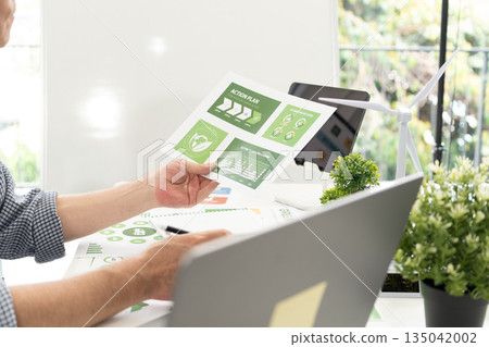 A diverse business team analyzing environmental charts and graphs in a collaborative meeting to create sustainable strategies in a modern office. 135042002