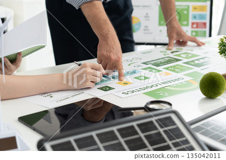 A diverse business team analyzing environmental charts and graphs in a collaborative meeting to create sustainable strategies in a modern office. 135042011