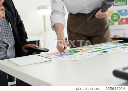 A diverse business team analyzing environmental charts and graphs in a collaborative meeting to create sustainable strategies in a modern office. 135042014
