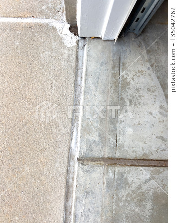 A concrete step beneath a doorway is shown with a sealed joint running across the surface. The lighting clearly reveals the texture and wear of the concrete area. 135042762