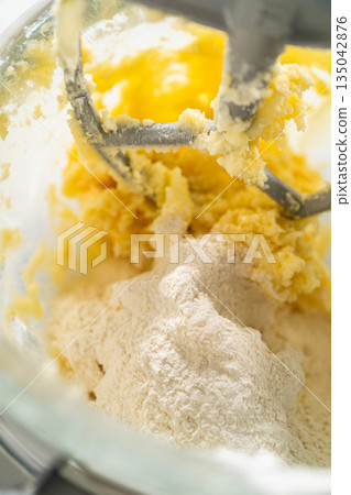 Close-up view of the stand mixer as dry ingredients are added to the wet mixture for Classic Sugar Cookie Dough. The flour is gently being incorporated into the butter, sugar, and eggs, creating the 135042876