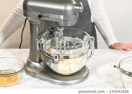 Front view of an electric stand mixer in use, blending ingredients for Classic Sugar Cookie Dough. The baker hands are steadying the bowl as the mixer combines butter, sugar, and other ingredients on 135042886
