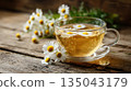A calming cup of chamomile tea surrounded by fresh daisies on a rustic wooden surface 135043179