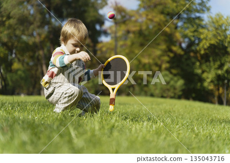 Toddler Child Playing Tennis with Racket in Sunny Park Toddler Child Playing Tennis with Racket in Sunny Park 135043716