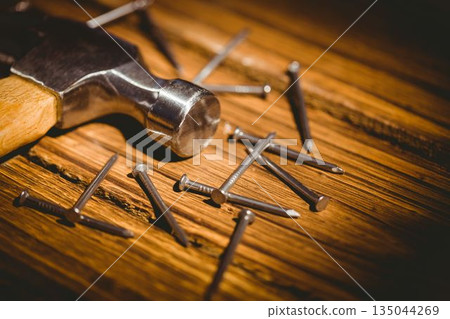 Flat design showing metallic hammer head with wooden handle resting on plank, featuring steel nails 135044269