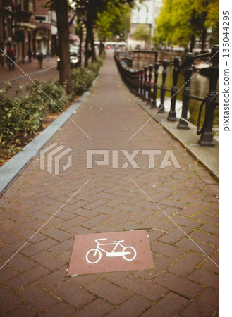 Red tile showing bicycle icon is marking flat design bike lane along brick canal with railing 135044295