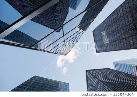 Office glass towers forming canyon at street level, reflecting sunlight on grid patterns 135044304