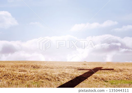 Flat design field is stretching under cloudy sky, showing cross-shaped shadow over golden stubble Flat design field is stretching under cloudy sky, showing cross-shaped shadow over golden stubble 135044311