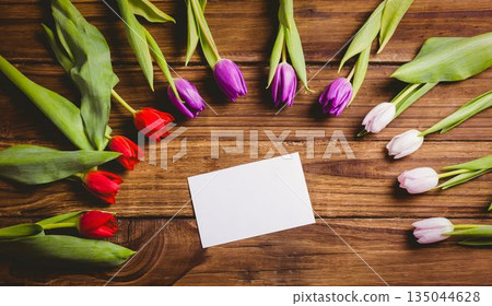 Blank white card is sitting on wooden tabletop in vector style, flanked by colorful tulip stems Blank white card is sitting on wooden tabletop in vector style, flanked by colorful tulip stems 135044628