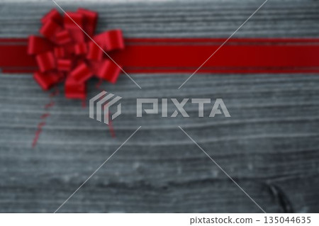 Red satin ribbon is stretching across grey wooden background with decorative bow, copy space 135044635