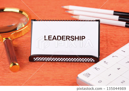 Card displays the word Leadership amidst a magnifying glass, pencils, and a calculator on a vibrant orange surface. A concept exploring direction, calculation, and vision Card displays the word Leadership amidst a magnifying glass, pencils, and a calculator on a vibrant orange surface. A concept exploring direction, calculation, and vision 135044989