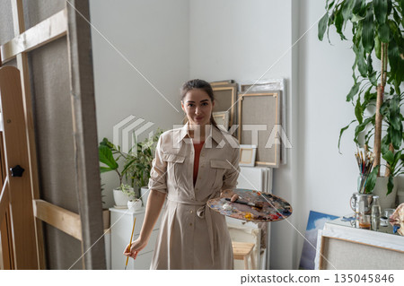 Confident cheerful female artist painting picture at creative home workshop, art hobby therapy. 135045846
