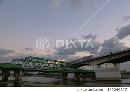黃昏時分，火車和公路車輛駛過鐵路橋。 135046327