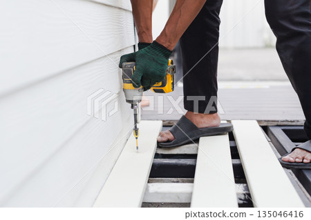A worker is using a cordless power drill to fasten exterior floor boards. A worker is using a cordless power drill to fasten exterior floor boards. 135046416