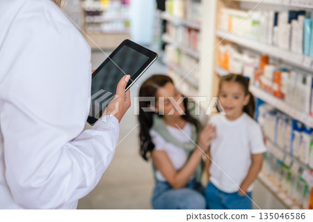 Pharmacist advising a young woman with a little girl on medicines 135046586