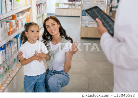 Pharmacist advising a young woman with a little girl on medicines 135046588