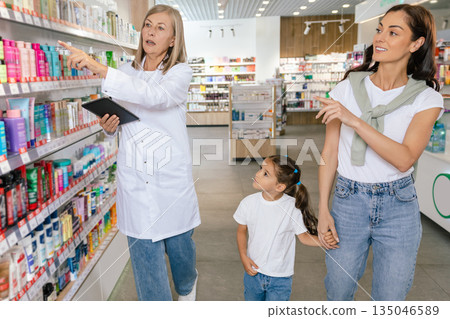 Pharmacist advising a young woman with a little girl on medicines Pharmacist advising a young woman with a little girl on medicines 135046589