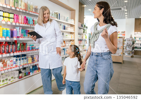 Pharmacist advising a young woman with a little girl on medicines Pharmacist advising a young woman with a little girl on medicines 135046592