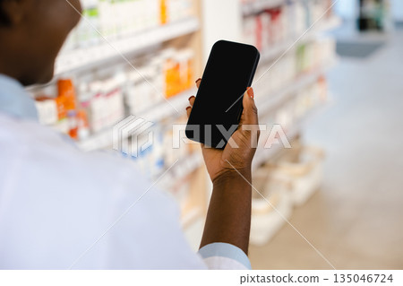 African american young woman in a lab coat holding a phone in her hands 135046724