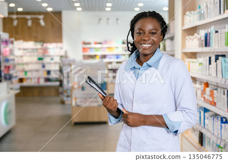 Dark-skinned young smiling female pharmacist in the drug store Dark-skinned young smiling female pharmacist in the drug store 135046775