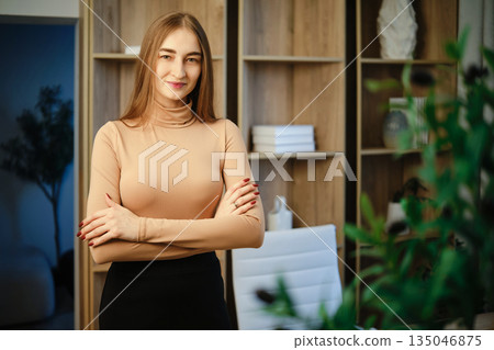 Woman stands in modern indoor environment with arms crossed, showcasing confidence and poise Woman stands in modern indoor environment with arms crossed, showcasing confidence and poise 135046875