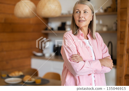 Mature woman standing in kitchen area with friendly smile Mature woman standing in kitchen area with friendly smile 135046915