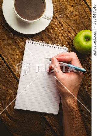 Cropped hand writing in book with coffee cup and apple on table Cropped hand writing in book with coffee cup and apple on table 135047140