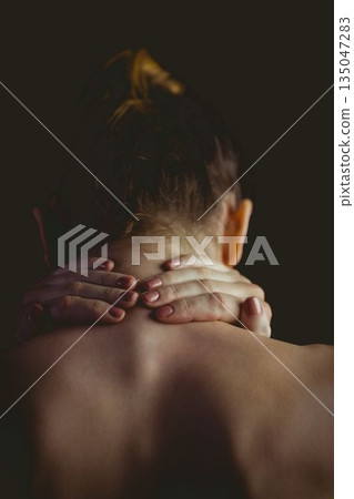 Female gripping and massaging neck in flat design showing bun, painted nails against dark backdrop 135047283