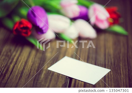 3D render showing blank white rectangular card on wooden tabletop featuring blurred tulip bouquet 135047301