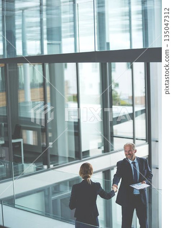 Smiling mature caucasian businessman shaking hands with female colleague in modern office Smiling mature caucasian businessman shaking hands with female colleague in modern office 135047312