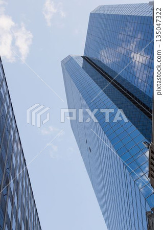 Showing flat blue glass skyscraper reflecting clouds beside mid-rise office building, copy space 135047322