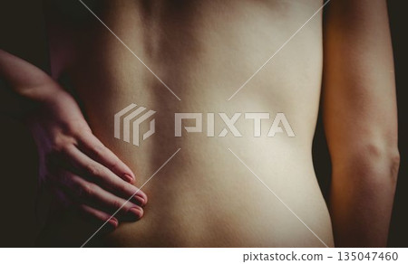 Bare female back is being shown in flat design illustration with soft lighting and dark backdrop 135047460
