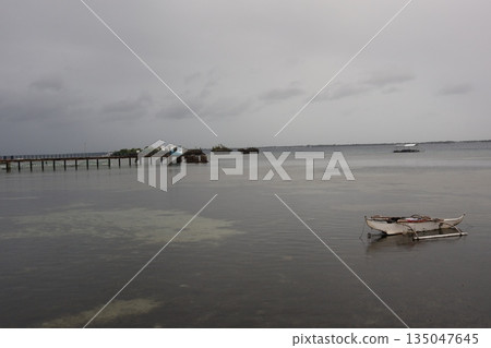 A beautiful ocean with underwater view, a pier, a small island, a boat, land on the opposite shore, and a cloudy sky. 135047645