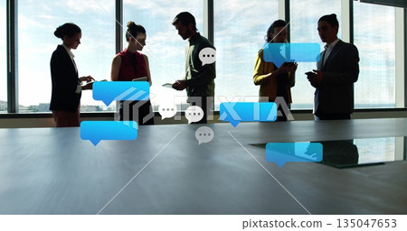 Standing business team chatting on smartphones and tablets in conference room, digital bubbles 135047653
