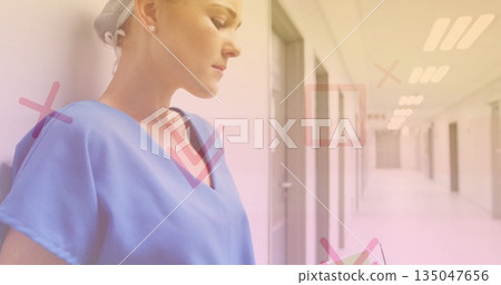 Holding tablet, nurse in blue scrubs reviewing records in ward corridor with overlays, copy space 135047656