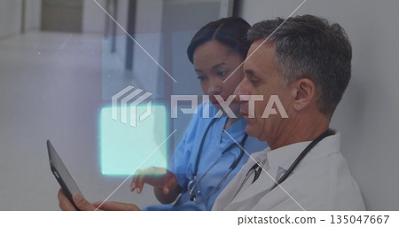 Reviewing tablet colleagues in scrubs and coats leaning against clinic hallway wall, copy space Reviewing tablet colleagues in scrubs and coats leaning against clinic hallway wall, copy space 135047667