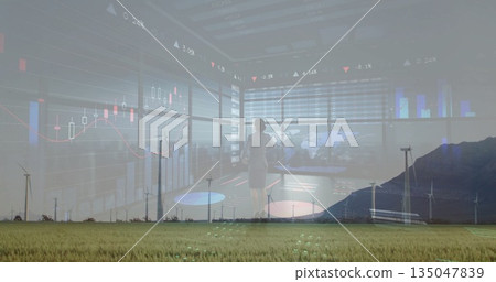 Observing executive scanning digital charts in glass hub, above grassy plain with wind turbines 135047839