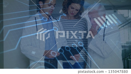 Holding tablet, doctors in white coats guiding patient in hospital corridor, with digital overlay 135047880
