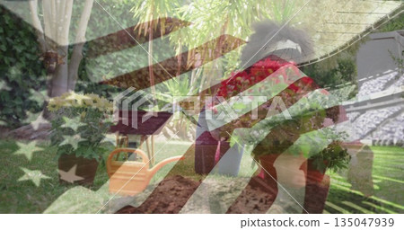 Kneeling girl planting potted flowers into soil in backyard, with orange watering can 135047939