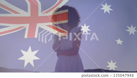 Standing woman wearing white lace dress on dawn hills, with translucent Australian flag overlay 135047948