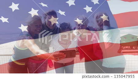 Leaning group of five women smiling viewing smartphone on boardwalk, with American flag overlay 135047955