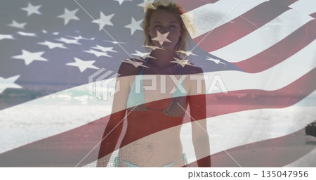 Walking woman in bikini along sandy shoreline with lapping ocean waves, with American flag overlay 135047956