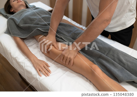 Masseur doing legs massage to a woman lying on a couch Masseur doing legs massage to a woman lying on a couch 135048380
