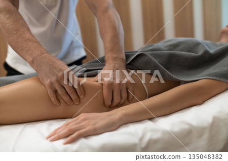Masseur doing legs massage to a woman lying on a couch 135048382