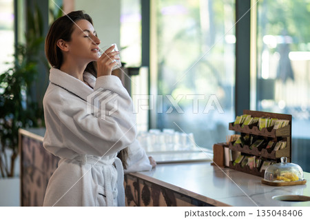Woman in white bathrobe drinking hot water with lemon Woman in white bathrobe drinking hot water with lemon 135048406