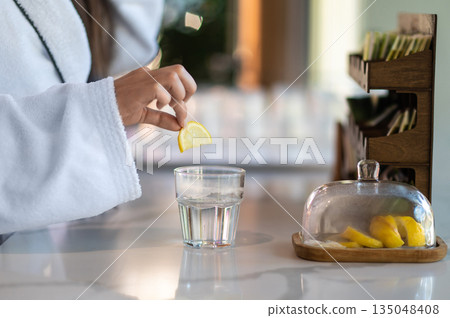 Woman in white bathrobe drinking hot water with lemon Woman in white bathrobe drinking hot water with lemon 135048408