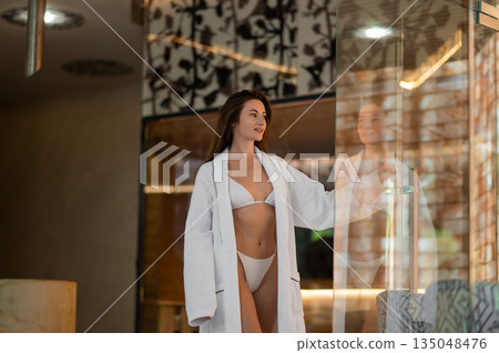 Pretty young woman in white robe in a spa center Pretty young woman in white robe in a spa center 135048476