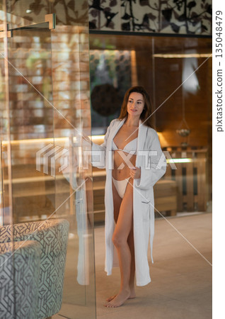 Pretty young woman in white robe in a spa center Pretty young woman in white robe in a spa center 135048479